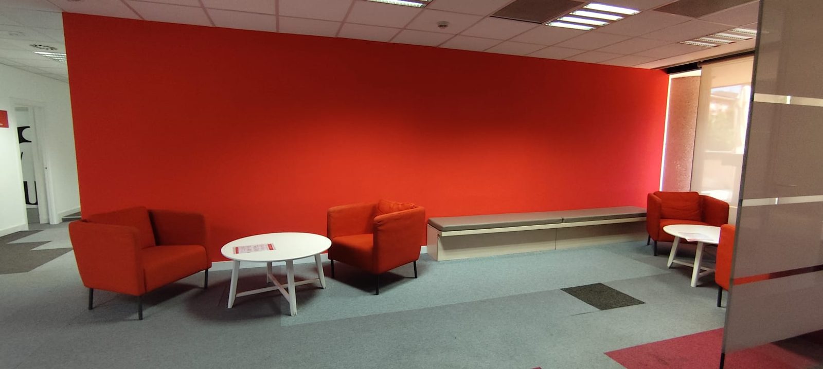 Zona de descanso con pared roja e iluminación LED en las oficinas de Save the Children en Madrid, reformadas por Buenos Días Buenas Noches